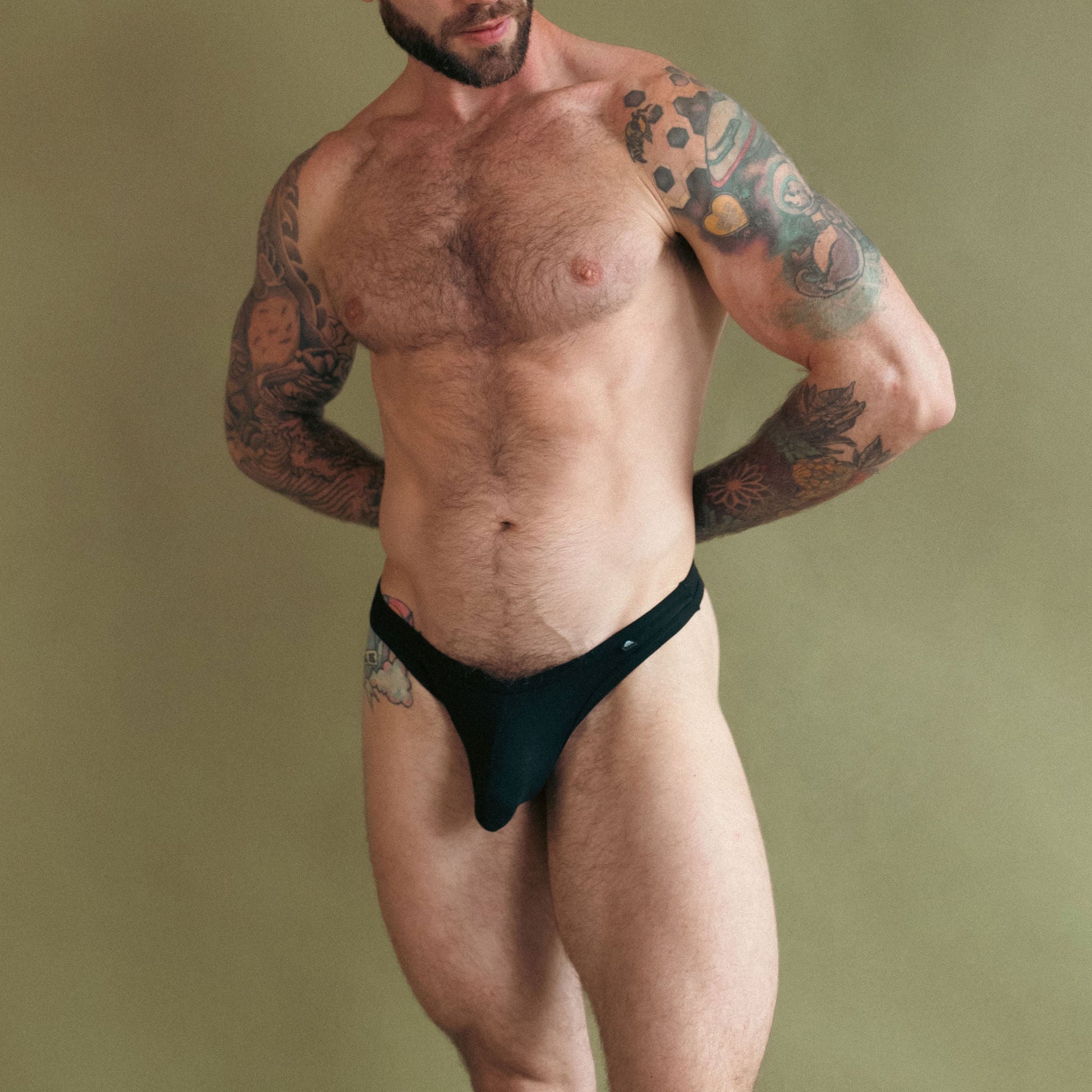 Man wearing a black thong against a beige background