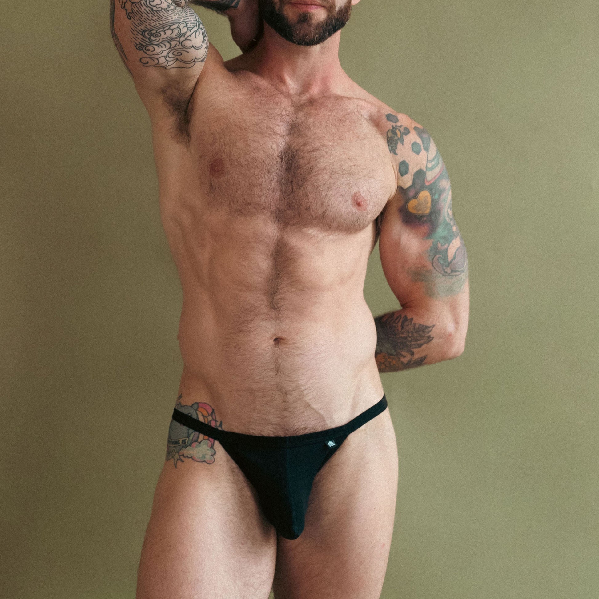 Man with tattoos wearing black underwear against a green background