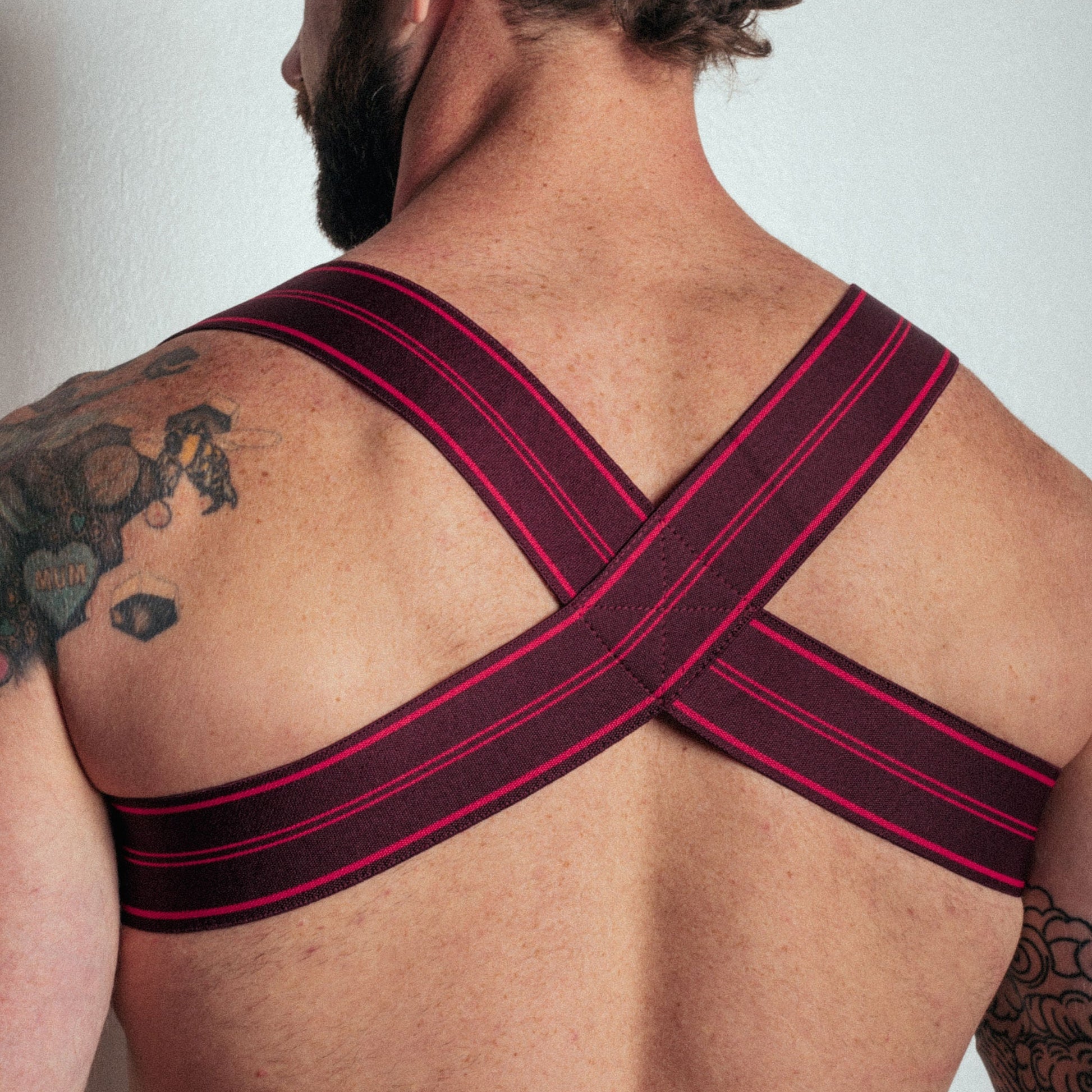 Man wearing a black and red strap across his back against a plain background