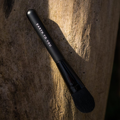 Black makeup brush with 'Earth to You' branding on a textured stone background