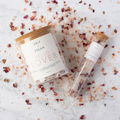 A jar and a refill tube of salts laying on a bed of salt and rose petals.