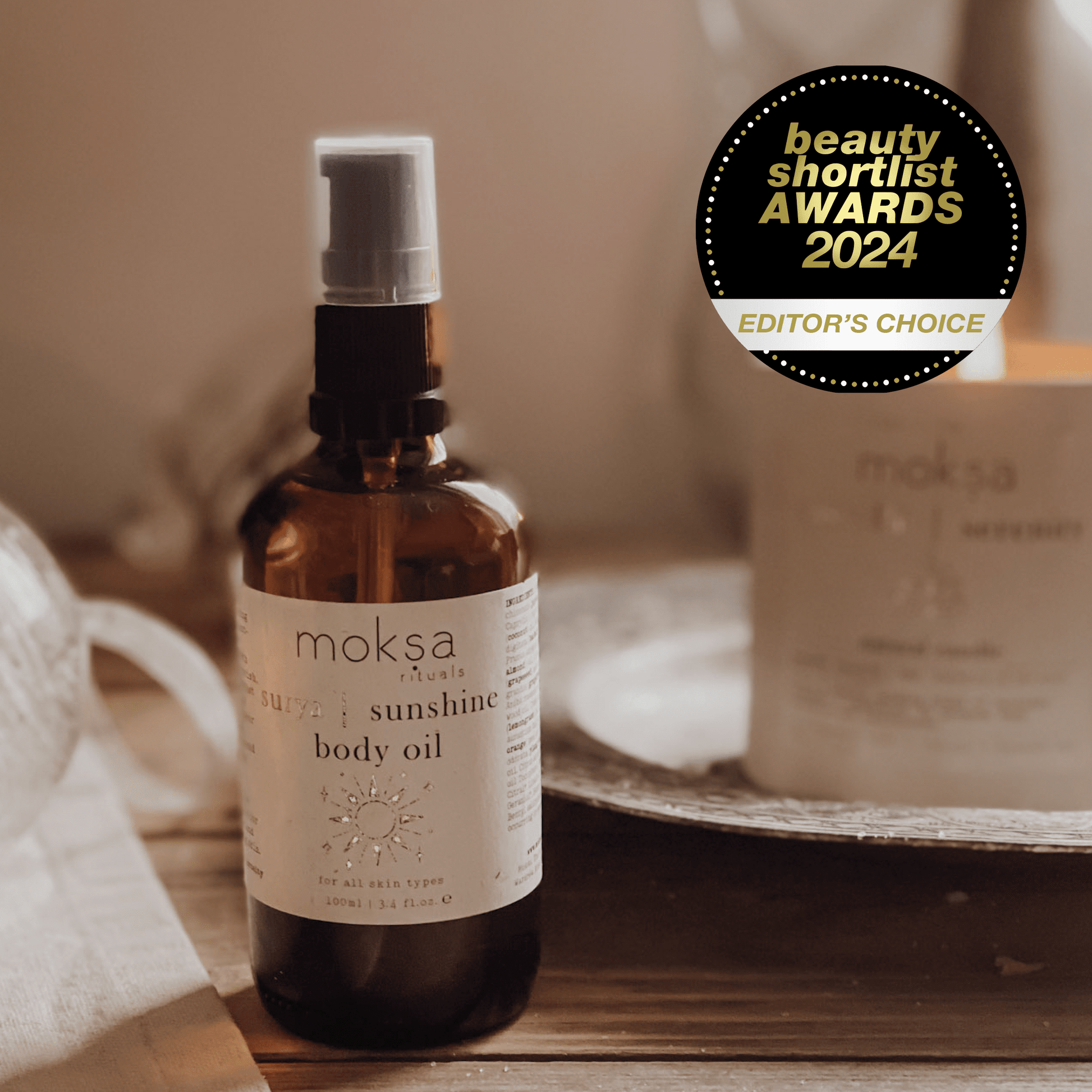 Bottle of body oil on a wooden table with a candle in the background.  Also an award sticker in the corner.