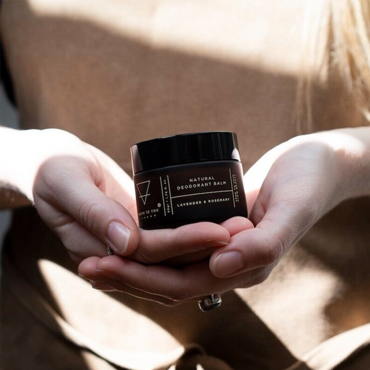 Person holding a black jar of natural deodorant balm with a blurred background