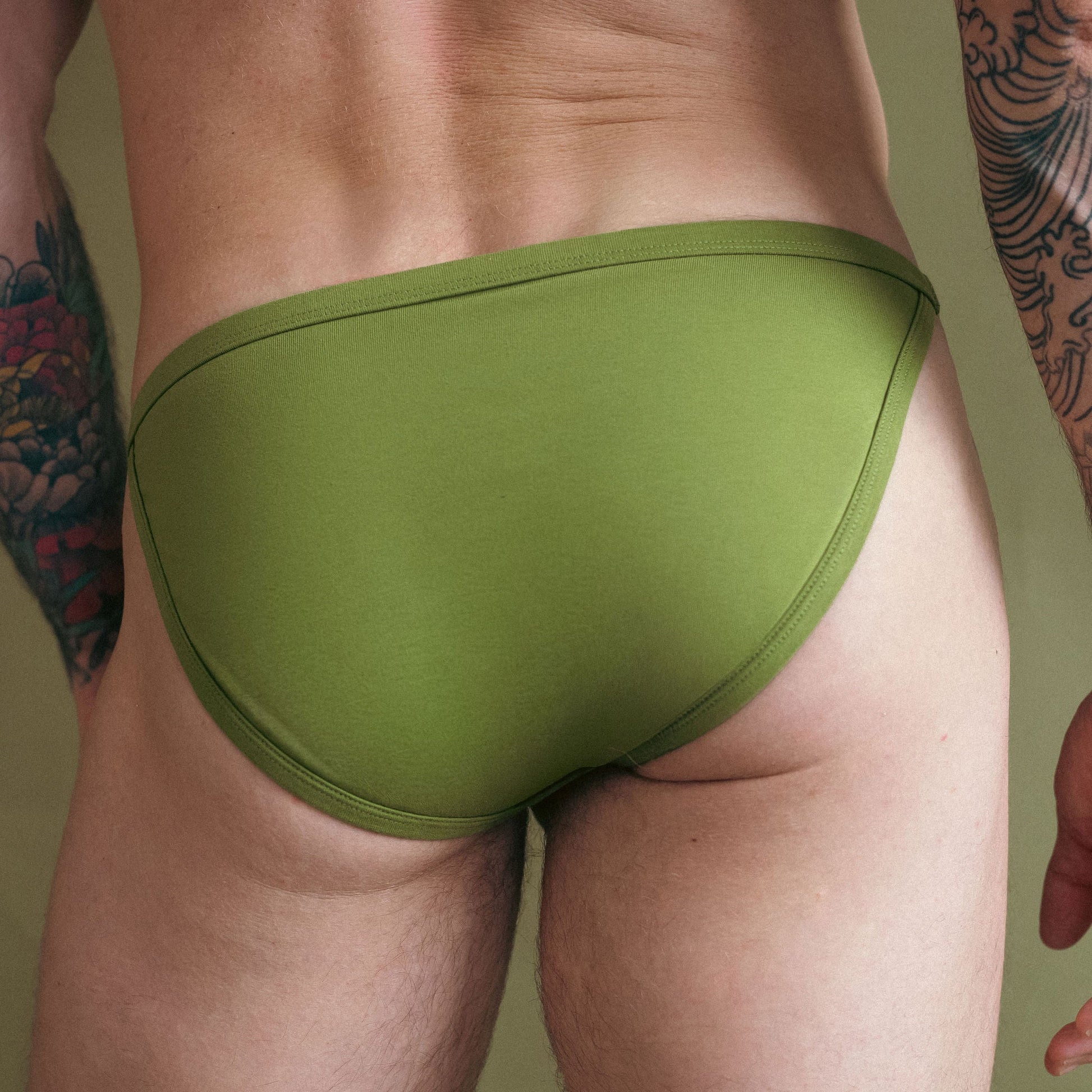 Green men's underwear on a person with tattoos against a neutral background