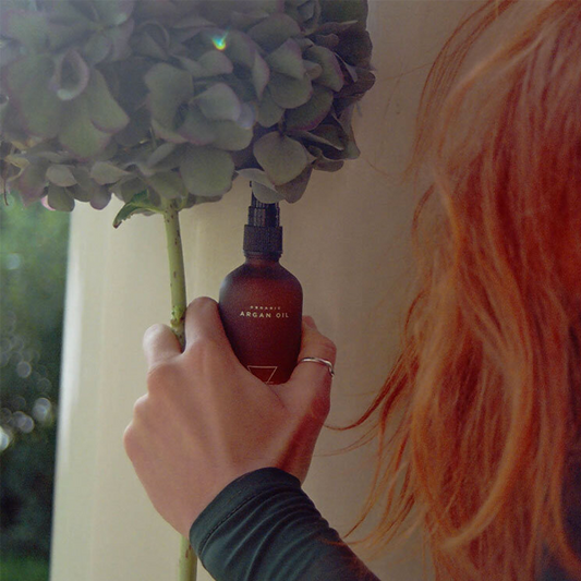Person holding a bottle of argan oil next to a flower