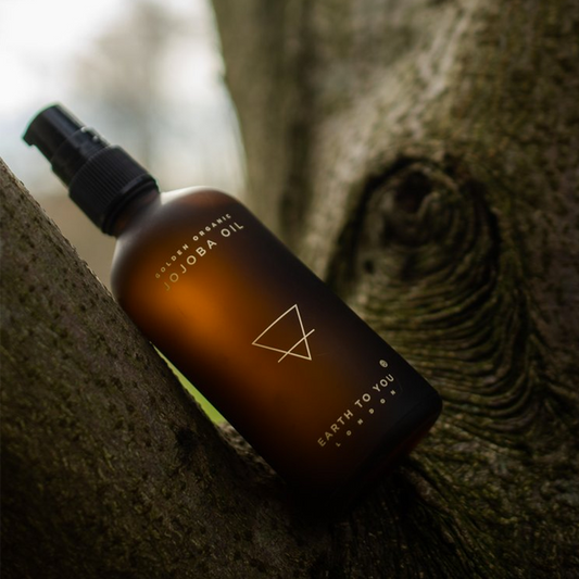 Bottle of jojoba oil with a black spray nozzle on a textured surface