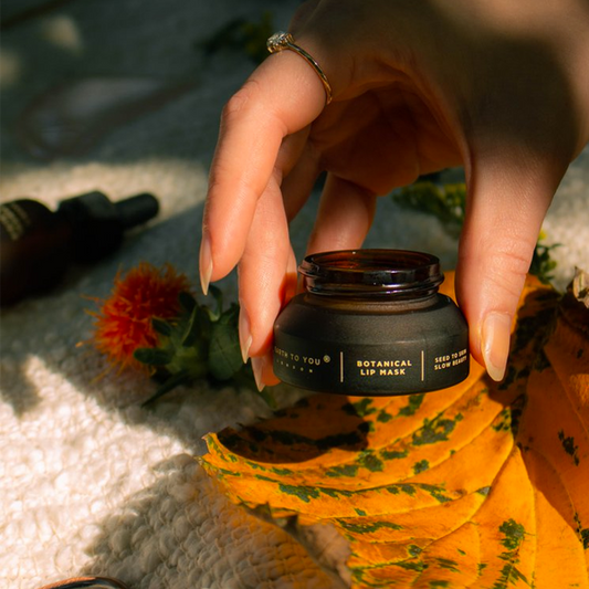 Person holding a black lip mask jar with floral and natural elements in the background