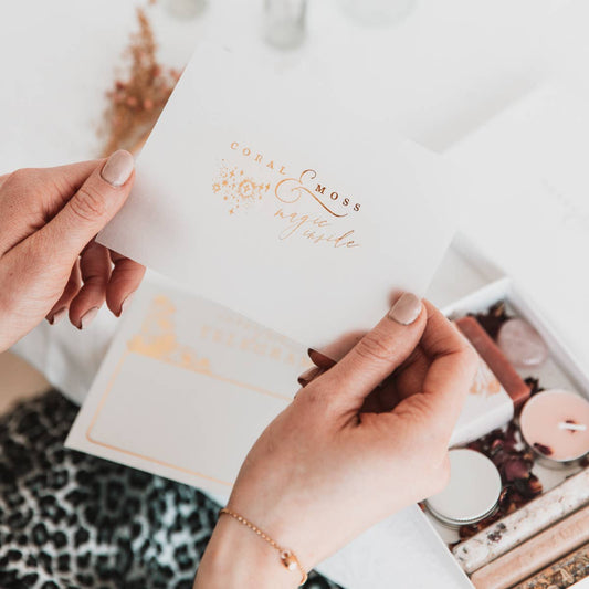A gift set and a branded card being held by a pair of hands from Coral and Moss