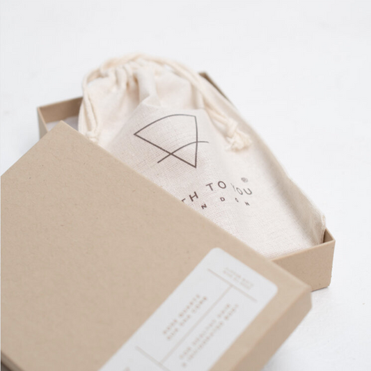 Beige drawstring bag with logo inside an open beige box on a white background