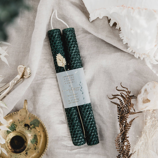 Moss Green candles laid on a cloth with a candle holder to the side and a candle stub.