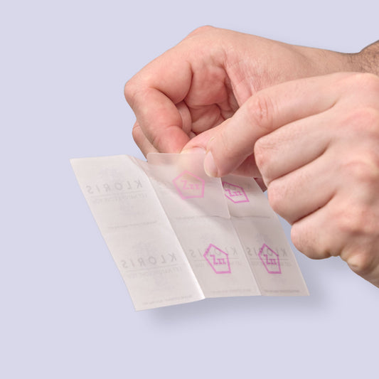 Hands holding a small white packet with pink logo on a light purple background