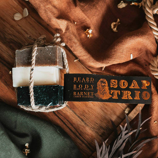 Trio of soap with tag laying on a table with cloth and leaves and rope.