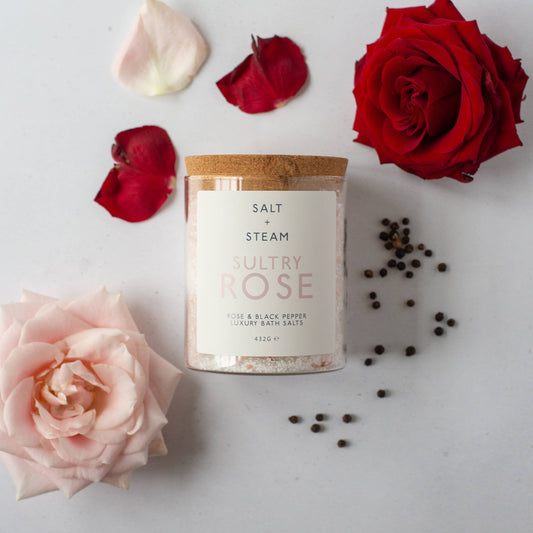Bath salt jar with rose scattered rose petals and peppercorns.