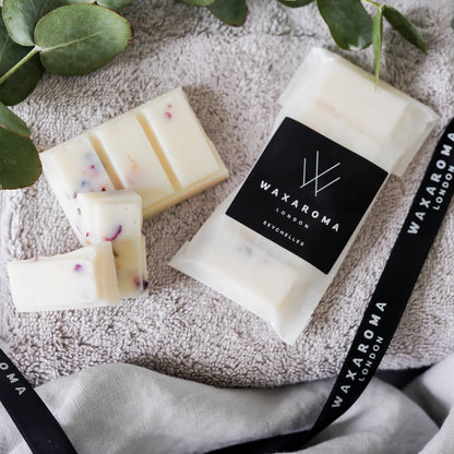 Packet of wax melts and pieces of wax melts on towel with branded ribbon and eucalyptus leaves