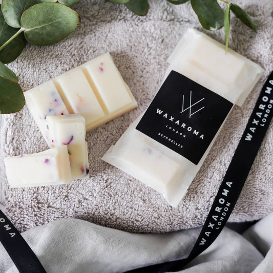 Packet of wax melts and pieces of wax melts on towel with branded ribbon and eucalyptus leaves