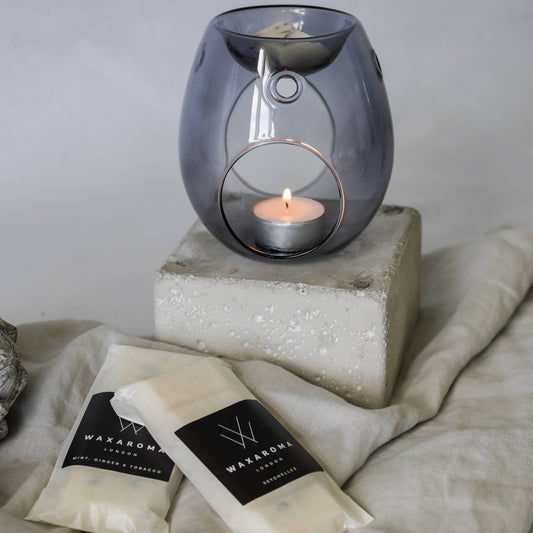 Two packets of waxaroma wax melts on a blanket and a wax melt burner with lit candle and wax melt inside