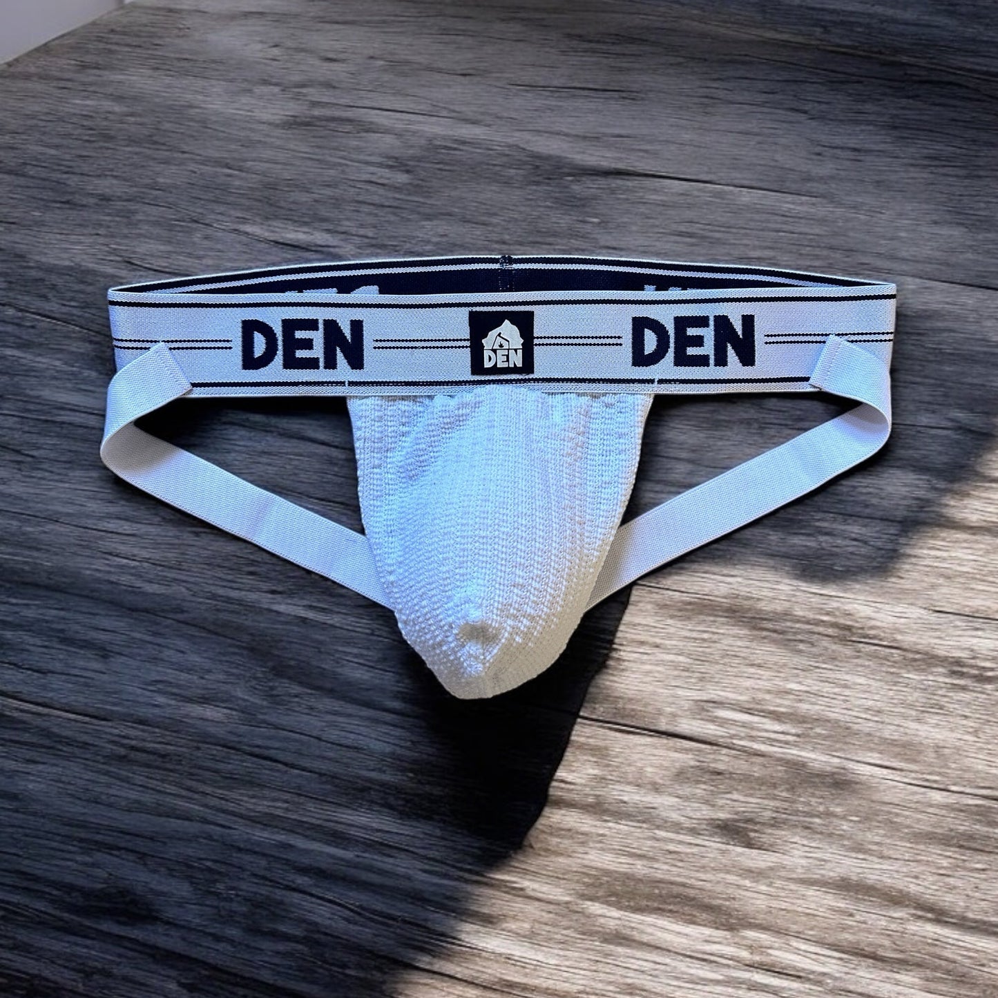 White men's underwear with 'DEN' branding on a wooden surface