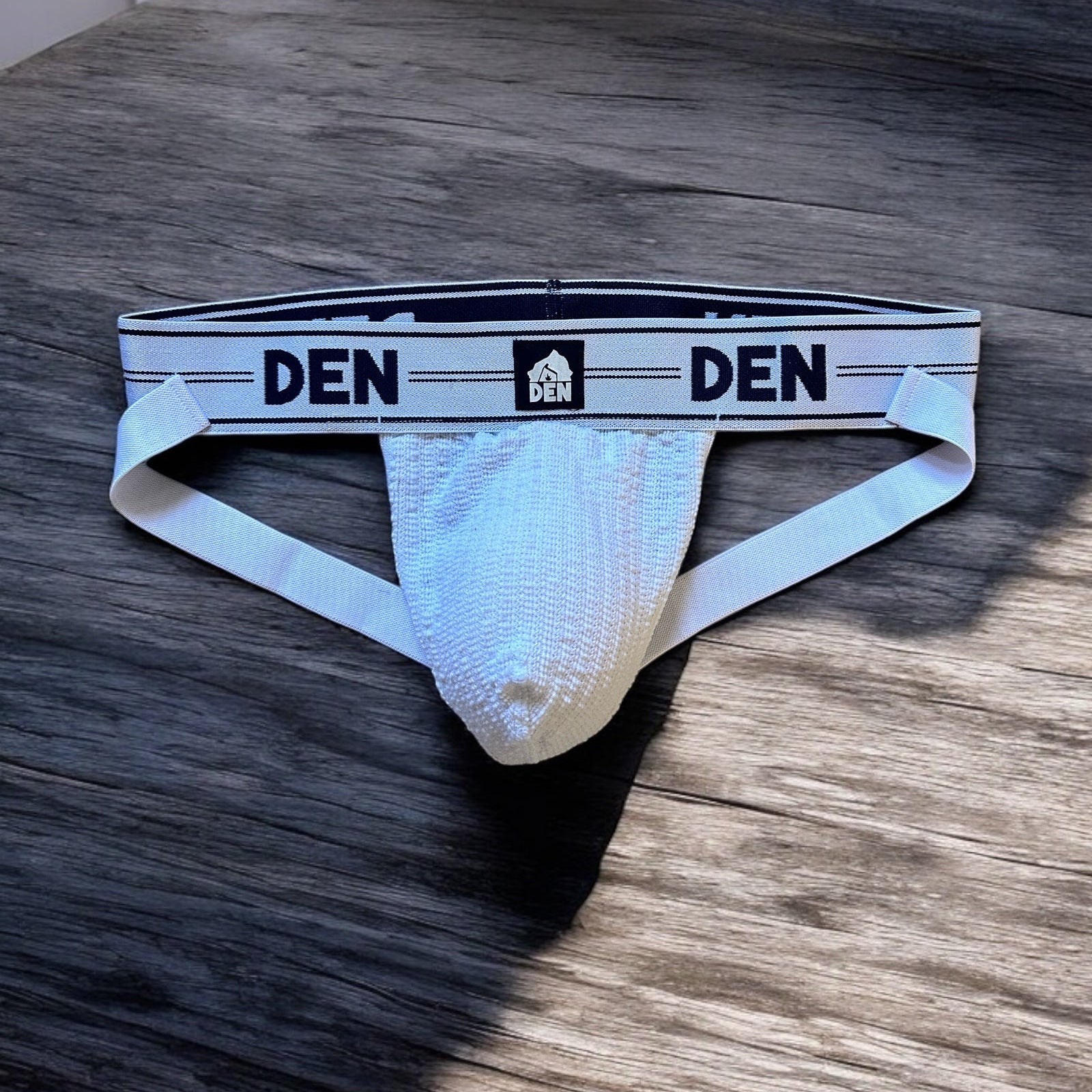 White men's underwear with 'DEN' branding on a wooden surface