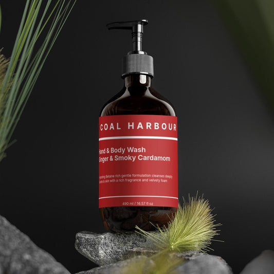 Bottle of Coal Harbour Ginger & Smoky Cardamom body wash on a dark background with greenery.