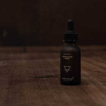 Black bottle labeled 'Sun Elixir Face' on a wooden surface with a dark background